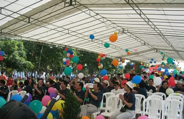 Large community event in Singapore with attendees gathered under a canopy, colourful balloons, event seating, and organised event planning activities.