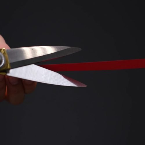 Hand with scissors cutting red ribbon opening ceremony concept. on black background.