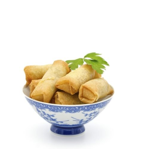 Bowl of vegetarian Thai spring rolls served with a spicy dipping sauce on a white background.